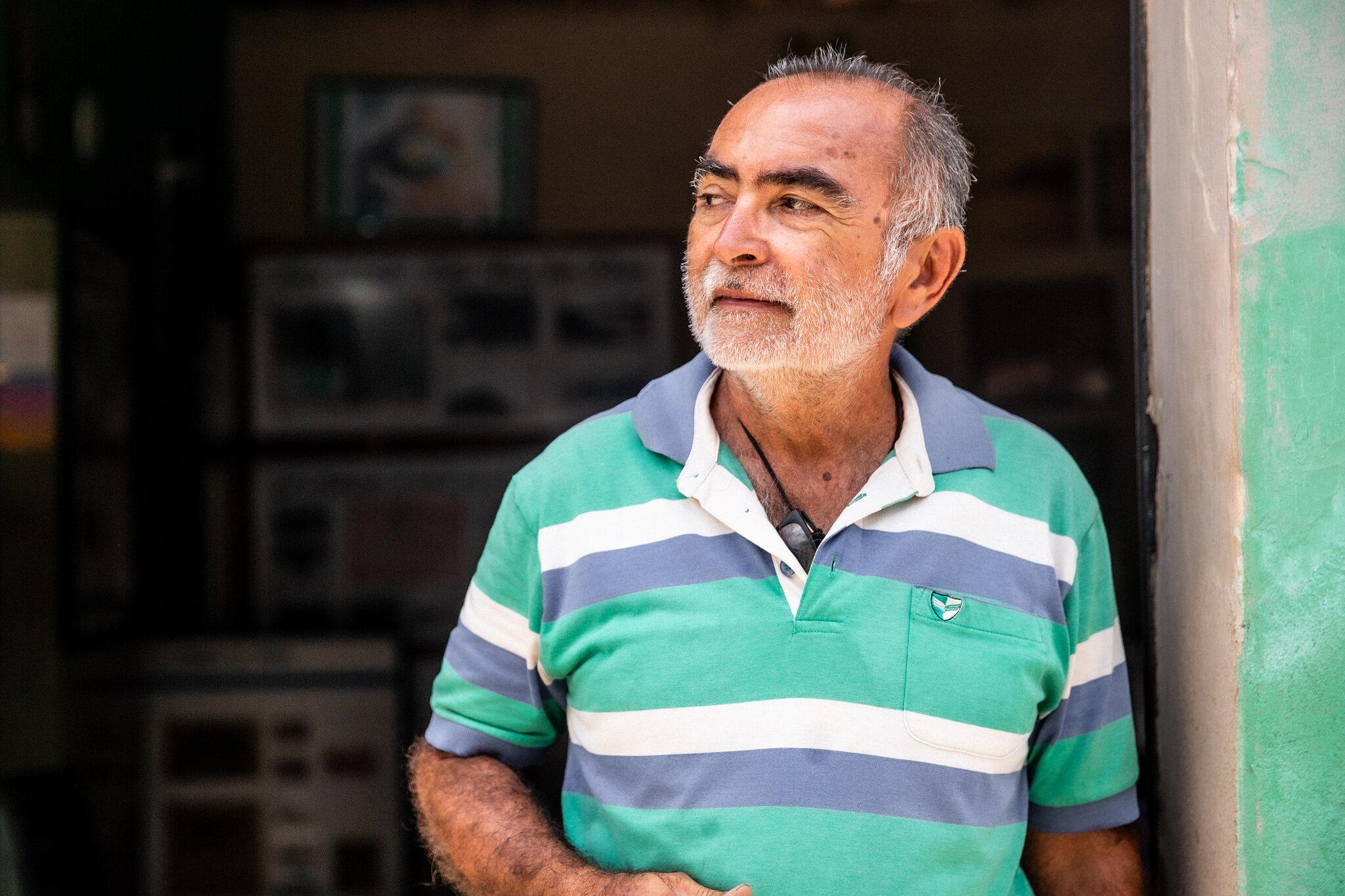 José Henrique Silva, comerciante, de blusa verde com listras brancas e azuis, olhando para o lado esquerdo