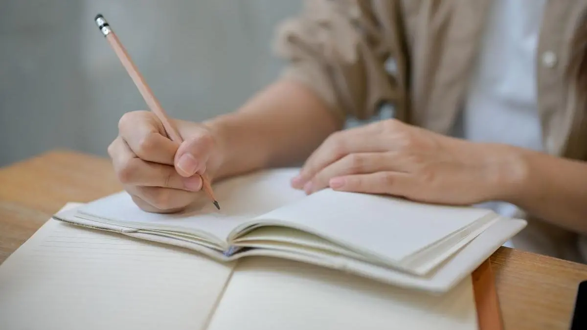 foto de aluno escrevendo com um lápis em caderno de folhas brancas
