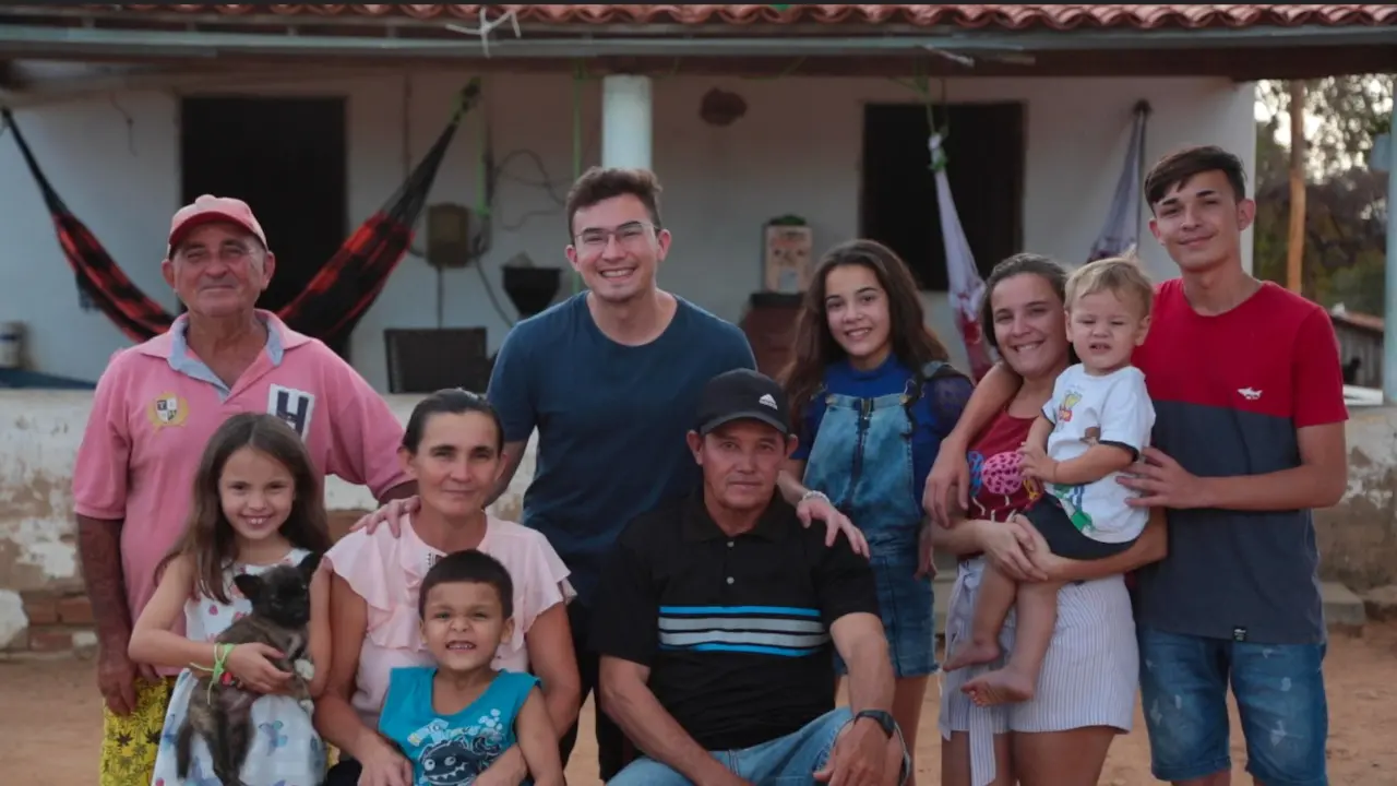 Na imagem, aparece o personagem ao lado da família Ao fundo, uma casa simples do interior do Ceará, com redes estendidas na varanda
