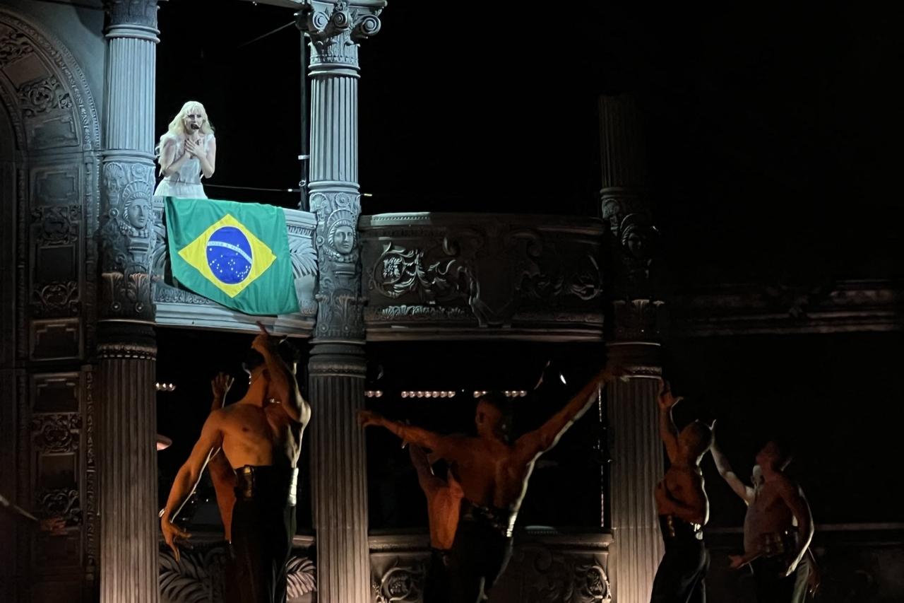 Lady gaga em palco com a bandeira do Brasil abaixo