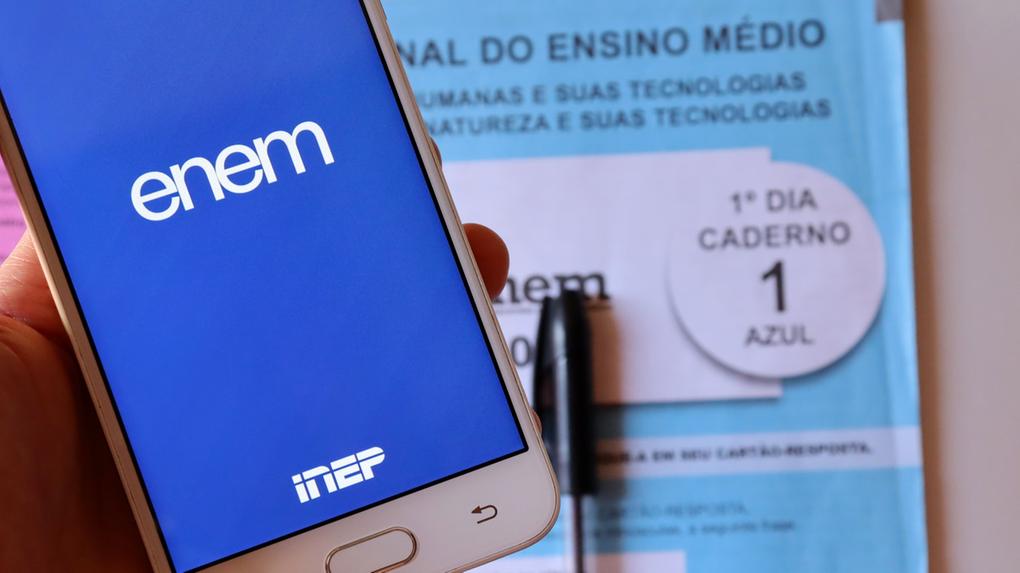 Imagem de um celular exibindo o aplicativo Enem do Inep. Em segundo plano, um caderno do Enem com detalhes de prova, ideal para estudantes do ensino médio.