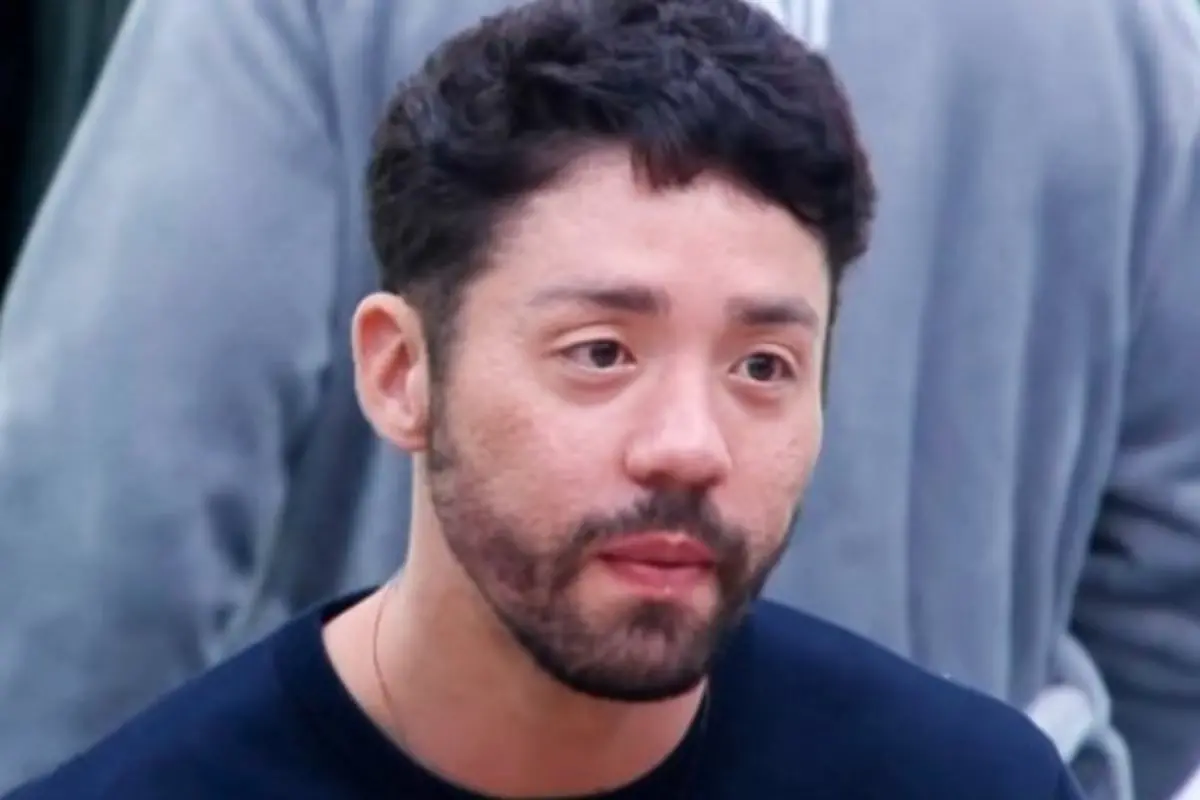 Imagem do participante do reality show Rico Melquíades, evidenciando sua expressão e estilo. Ele possui cabelo curto e barba, transmitindo um olhar pensativo.