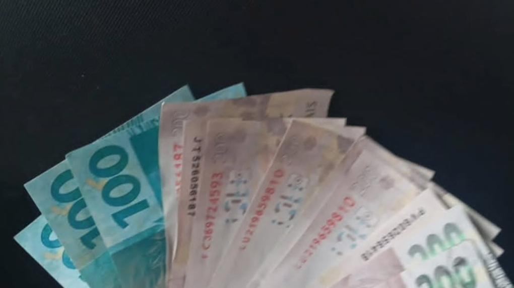 Notas de dinheiro em um punho, incluindo cédulas de 100 e 200 reais, representando riqueza e transações financeiras no Brasil.