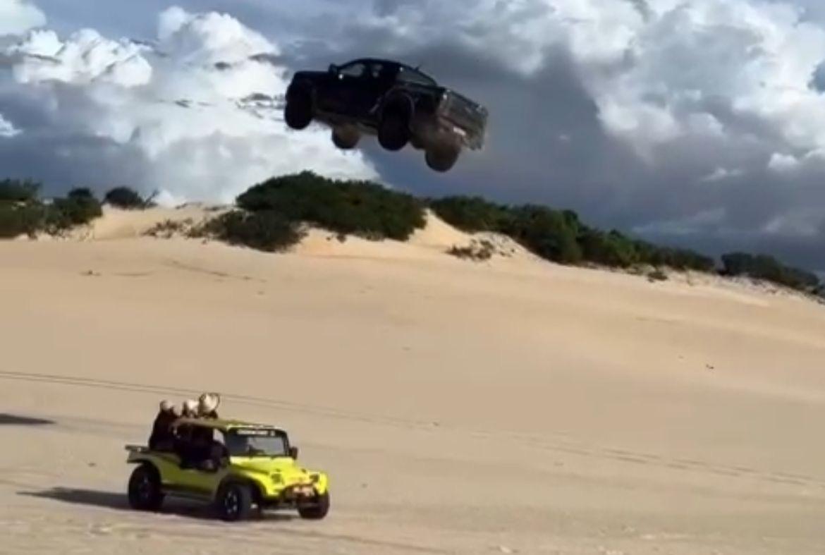 Foto que contém um carro em pleno ar após pular uma duna em Canoa Quebrada. Abaixo, um buggy amarelo