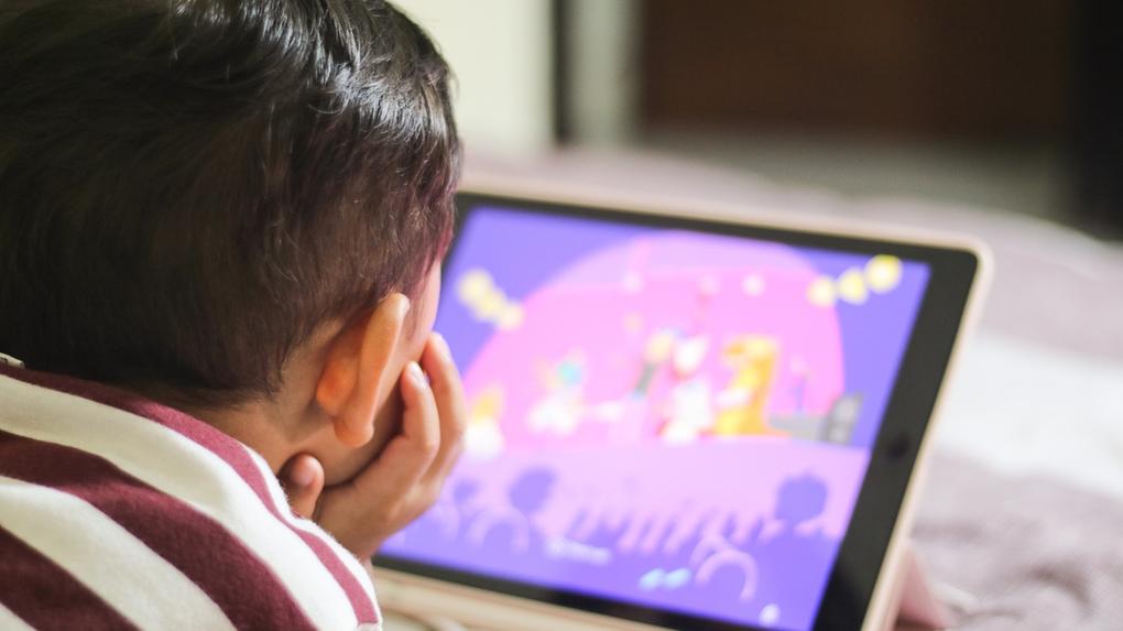 Imagem mostra bebê assistindo vídeo em tablet deitado em cama, ilustrando novo exame que identifica autismo em 15 minutos