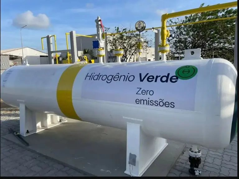 Foto que contém um equipamento cilíndrico na cor branca na horizontal sustentado por pés de metal com um adesivo afixado com os dizeres 