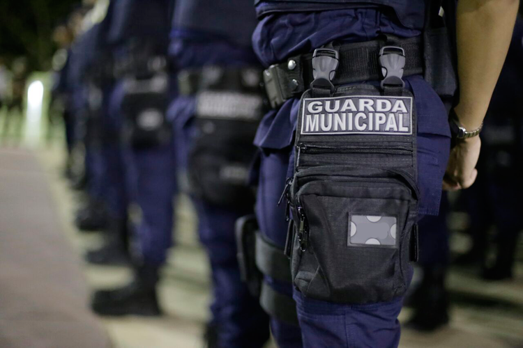 Guarda Municipal vestida com uniforme policial e equipado com bolsas e ferramentas, durante uma operação de segurança urbana.