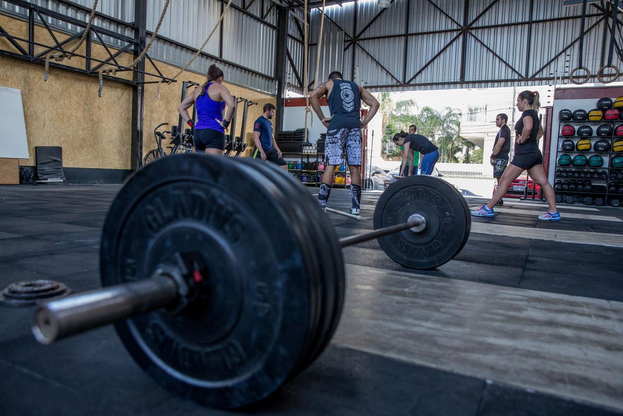 Foto que contém ambiente de box de crossfit com alunos ao fundo. Em primeiro plano, haltere feito para exercício de crossfit para matéria especial sobre apps de bem-estar