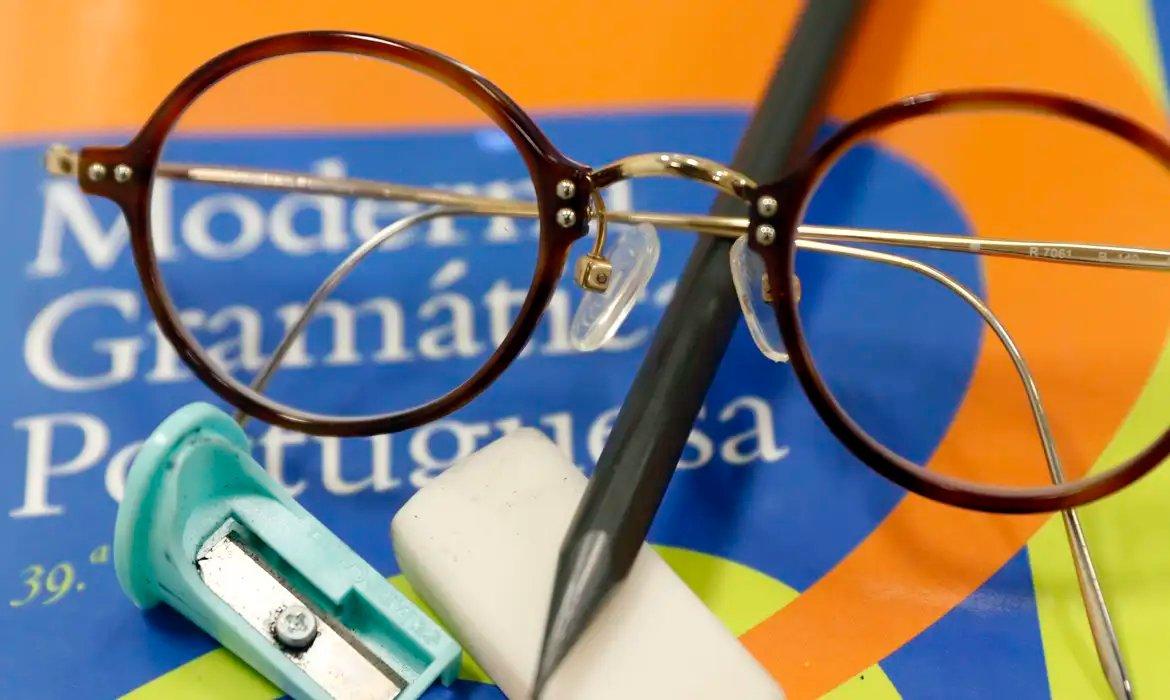 Um livro com óculos, lápis e apontador sobre ele