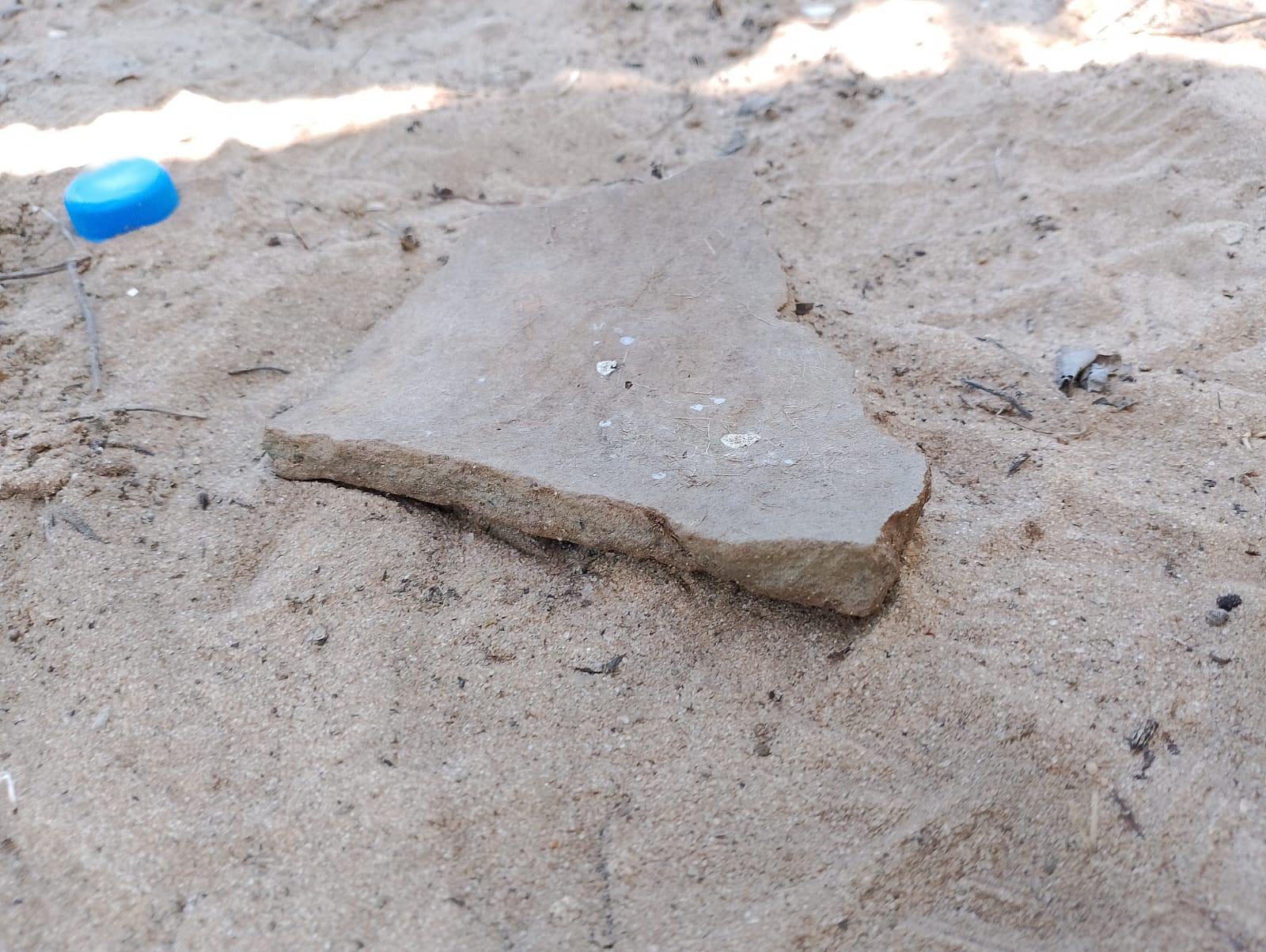 Imagem mostra um pedaço de cerâmica antiga, ao lado dela uma tampa de garrafa de plástico usada para dar dimensão do tamanho da peça arqueológica