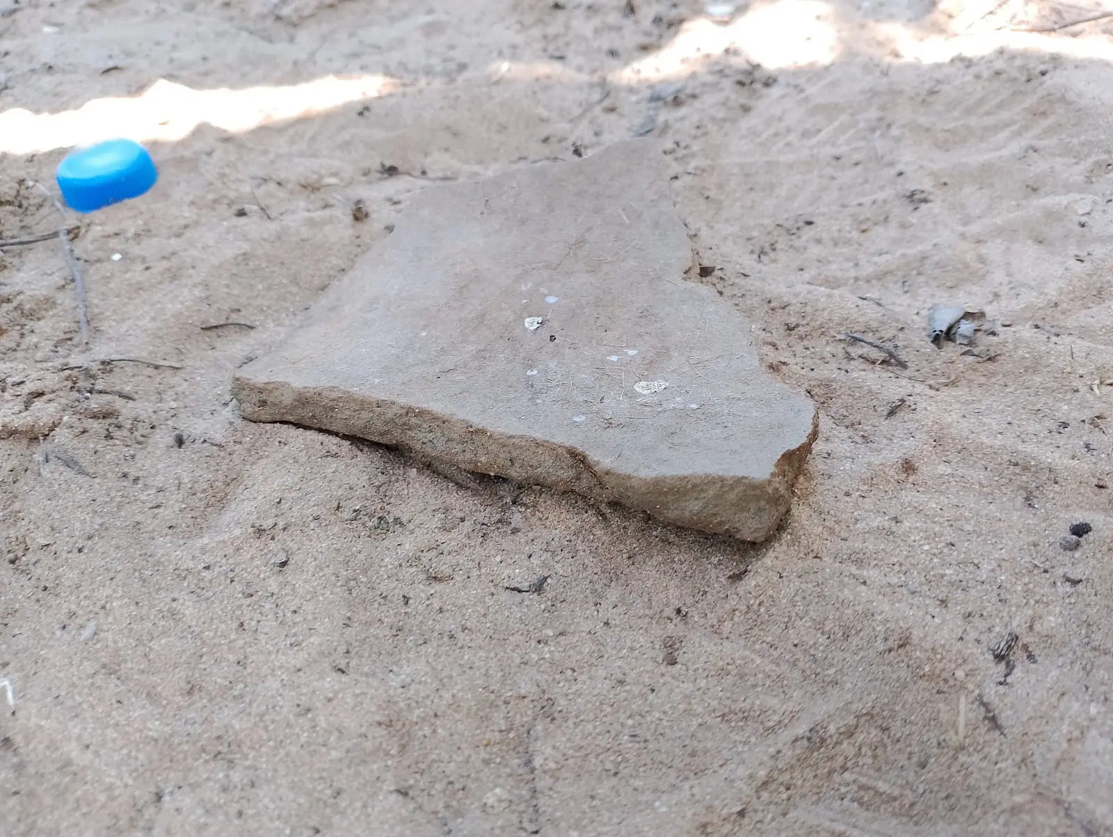 Imagem mostra um pedaço de cerâmica antiga, ao lado dela uma tampa de garrafa de plástico usada para dar dimensão do tamanho da peça arqueológica