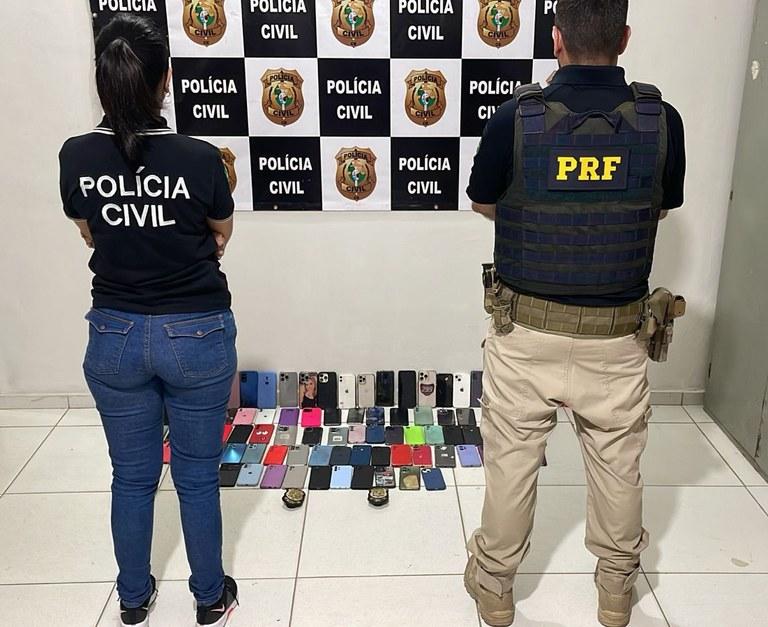 Imagem de dois agentes policiais, um da Polícia Civil e outro da Polícia Rodoviária Federal, com diversos celulares recuperados