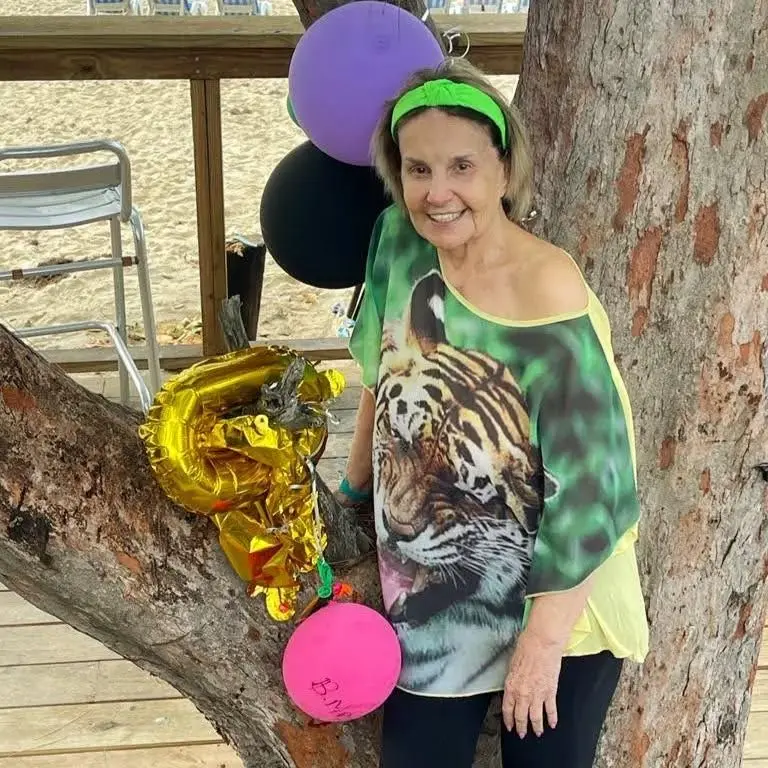 Íris Bruzzi diante de uma árvore. ela veste roupa verde e tem uma faixa verde no cabelo. atriz participou da primeira versão de vale tudo