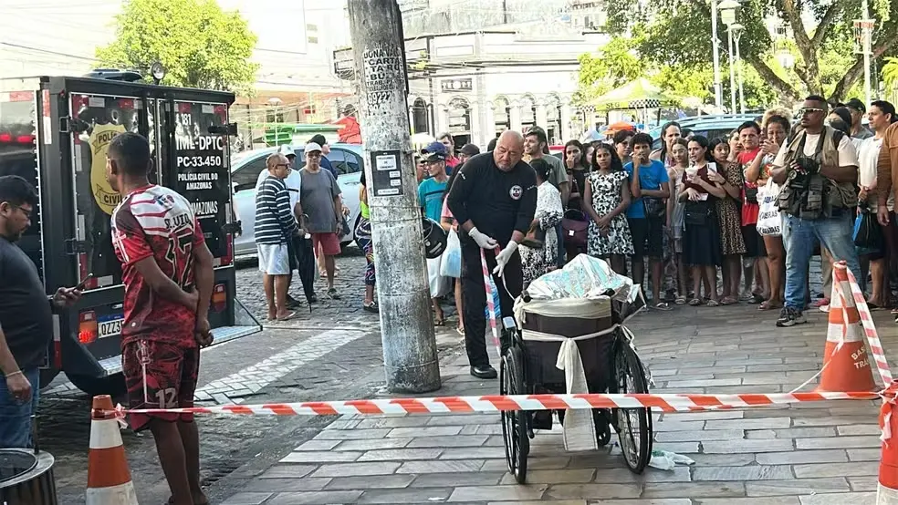 imagem mostra idoso morto na cadeira de rodas e área isolada com pessoas em volta