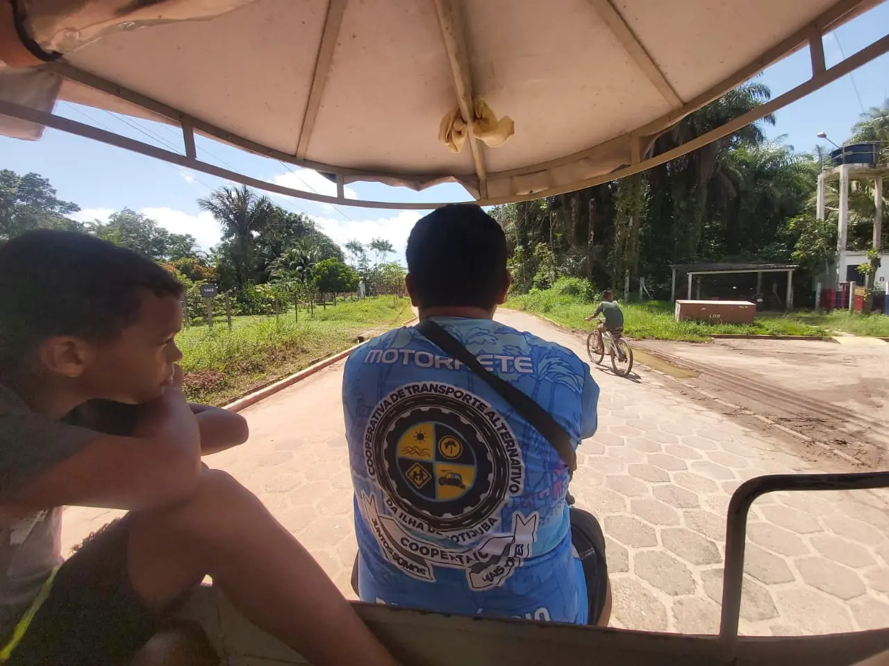 Na imagem, aparece uma criança olhando para o lado e um home pilotando uma 'motorrete'