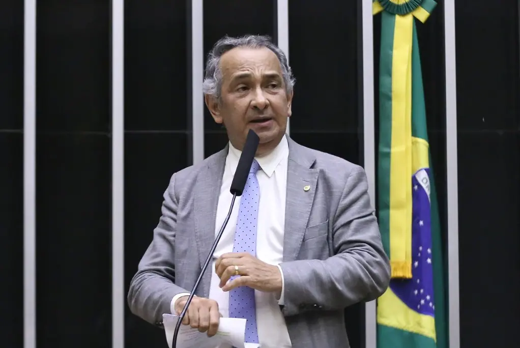 A imagem mostra o deputado federal Dr. Jaziel na tribuna do plenário da Câmara dos Deputados. Ele tem cabelos grisalhos e pele branca. Veste um terno cinza, uma gravata azul-claro e uma camisa branca. Está falando ao microfone.