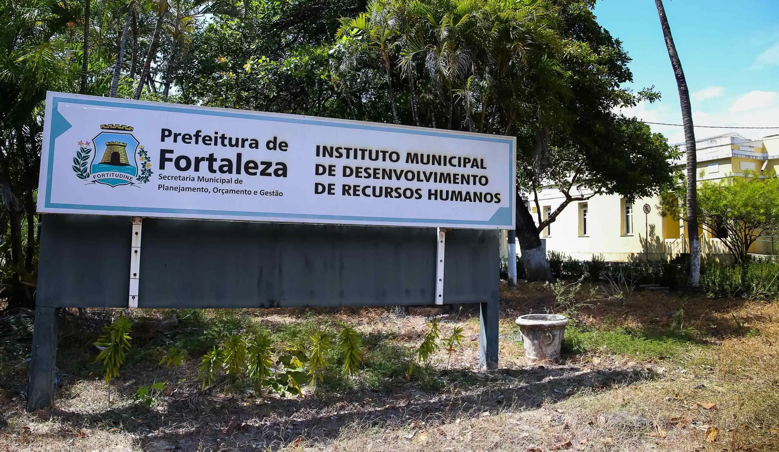 Placa de identificação da Prefeitura de Fortaleza indicando o Instituto Municipal de Desenvolvimento de Recursos Humanos, ao ar livre com árvores ao fundo.