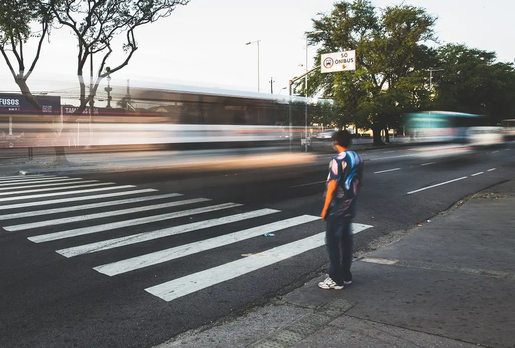 Foto de homem esperando para atravessar na faixa de pedestres enquanto ônibus passam em alta velocidade na Avenida Bezerra de Menezes, em Fortaleza