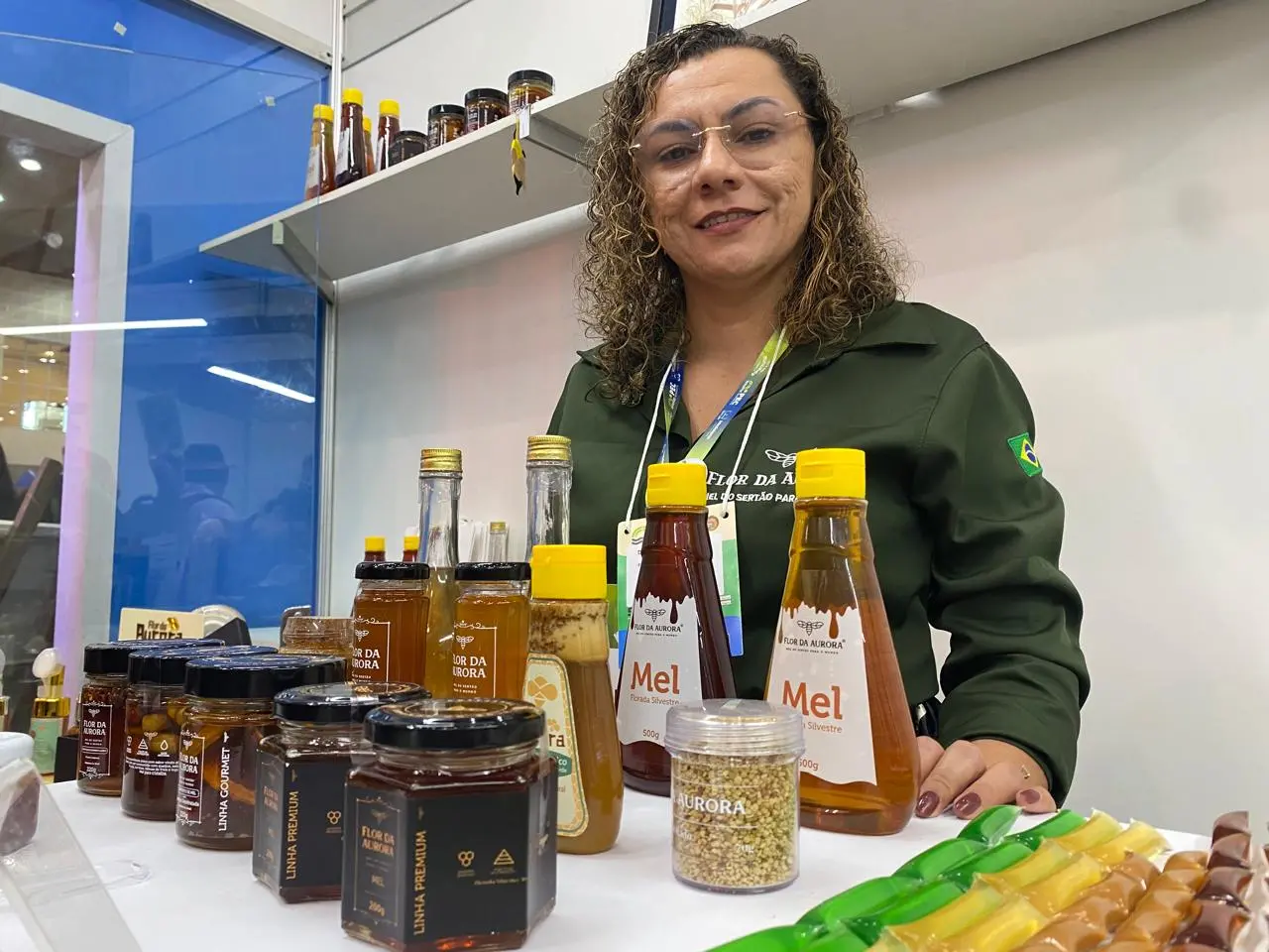 Imagem mostra uma mulher chamada Dina Pereira com os produtos de sua marca, Flor da Aurora