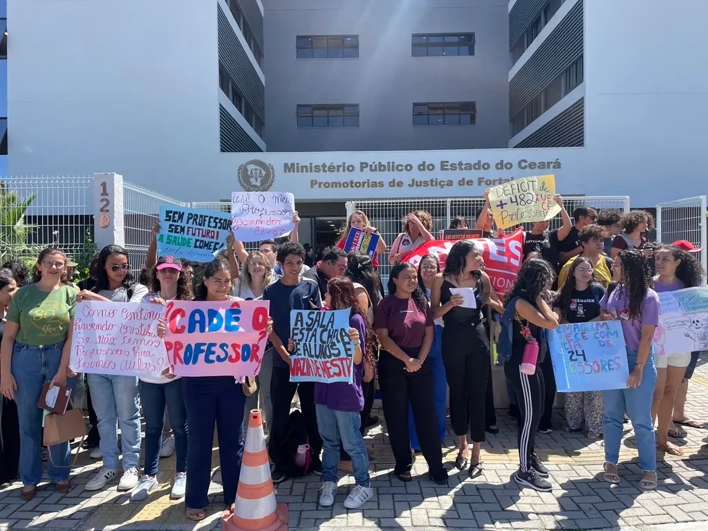 Foto de alunos e professores da Uece protestando em frente ao Ministério Público de Fortaleza segurando faixas e cartazes pedindo mais professores
