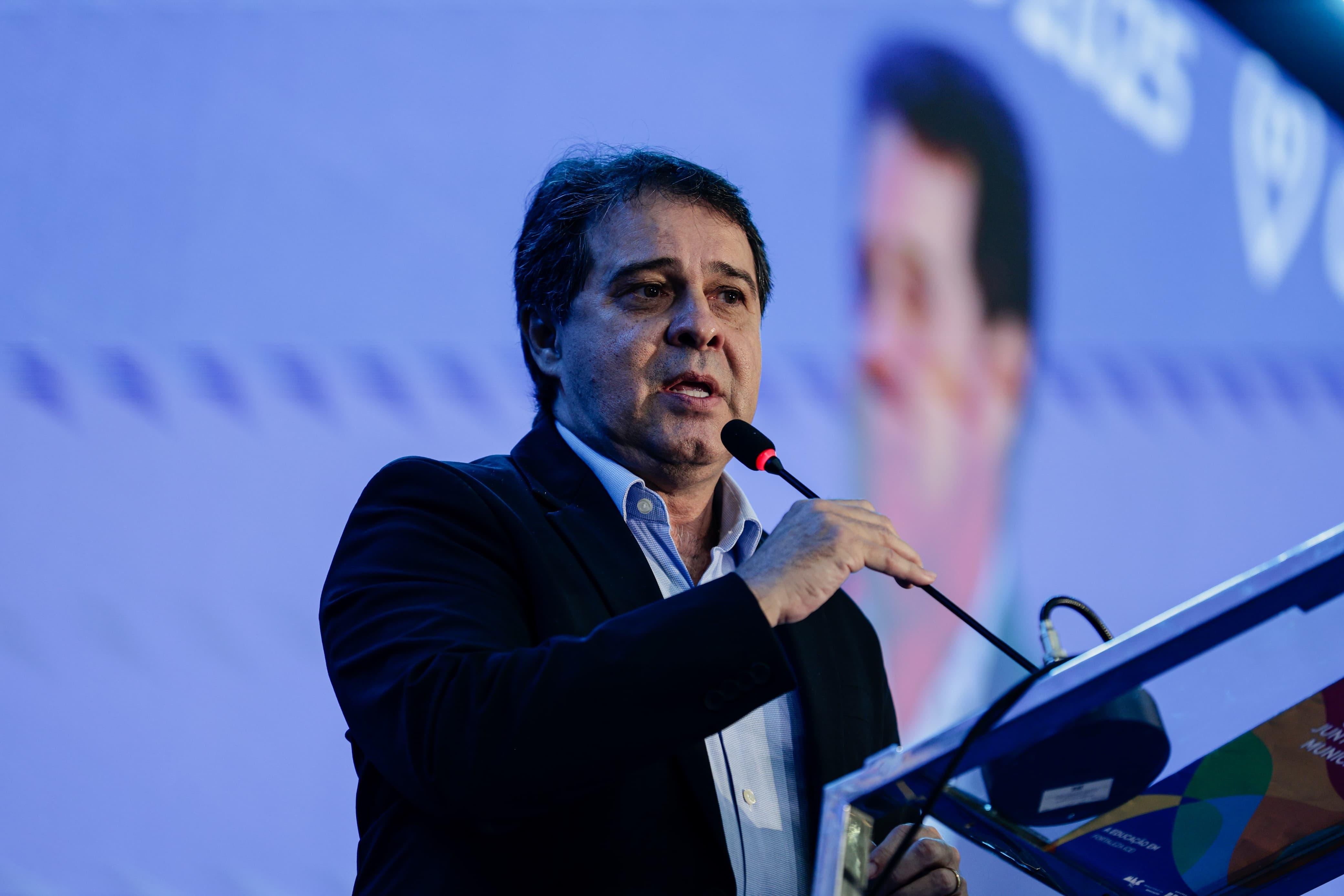 A imagem mostra Evandro Leitão durante discurso no Seminário dos Prefeitos, no Ceará. Ele veste um terno escuro e uma camisa azul clara. Seus cabelos são castanhos e sua pele, branca.