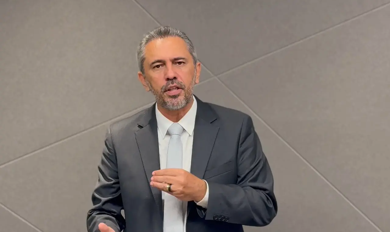 Foto de Elmano de Freitas usando terno com gravata cinza em um fundo cinza. No vídeo ele fala sobre uma reunião com o BNDES e anuncia investimento para o Ceará