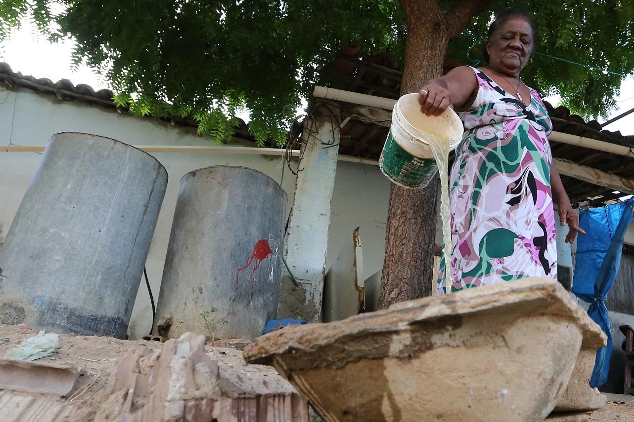Foto de mulher negra com vestido colorido derrama água de balde dentro de outro reservatório devido à falta de água na cidade de Milhã, no Ceará
