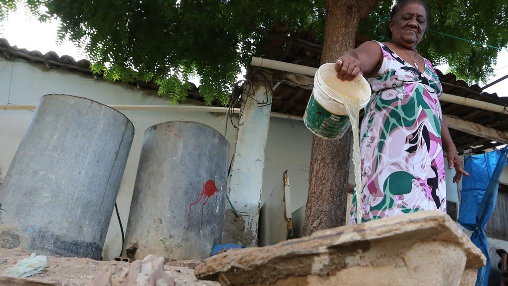 Foto de mulher negra com vestido colorido derrama água de balde dentro de outro reservatório devido à falta de água na cidade de Milhã, no Ceará