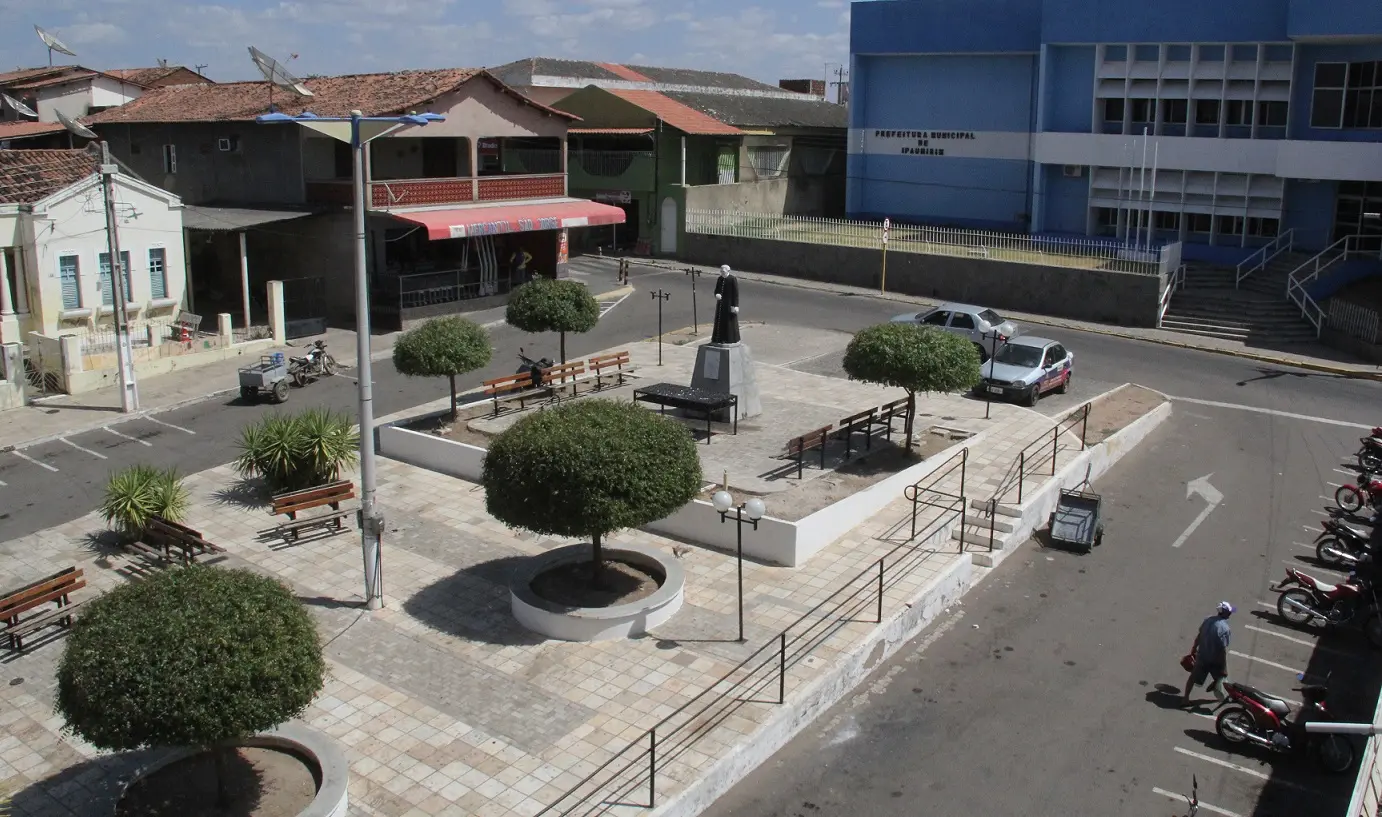 Foto aérea da praça central da cidade de Ipaumirim, no Ceará, com árvores, motocicletas e uma estátua central de Padre Cícero
