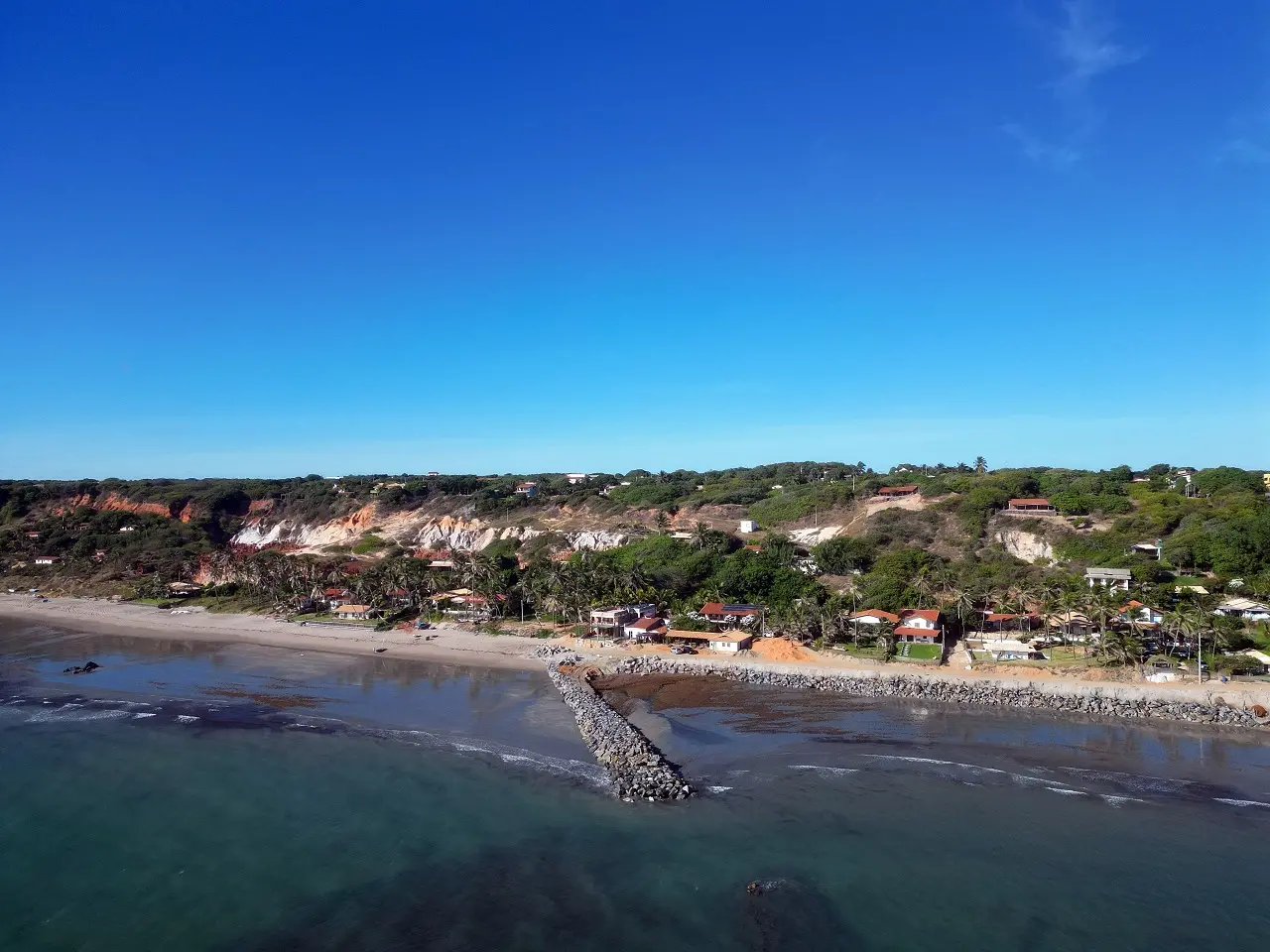 Foto aérea da costa da praia da Peroba, em Icapuí, mostrando espigão em construção, coqueiros, residências e pousadas ameaçadas pelo avanço do mar