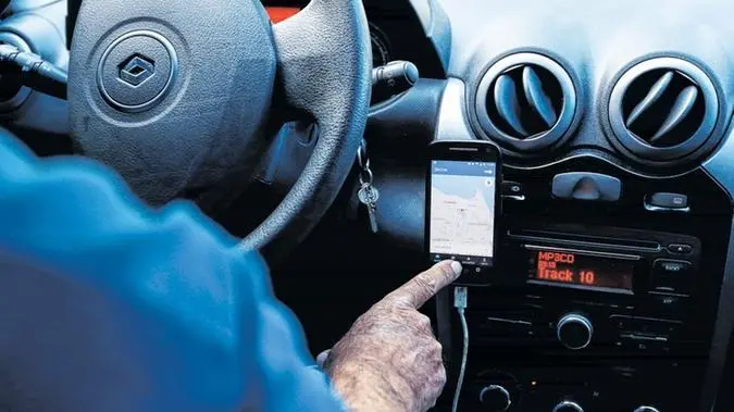 Imagem mostra homem manuseando o mapa de um aplicativo de corrida, dentro de um carro. Utilizada para ilustrar matérias sobre o assunto