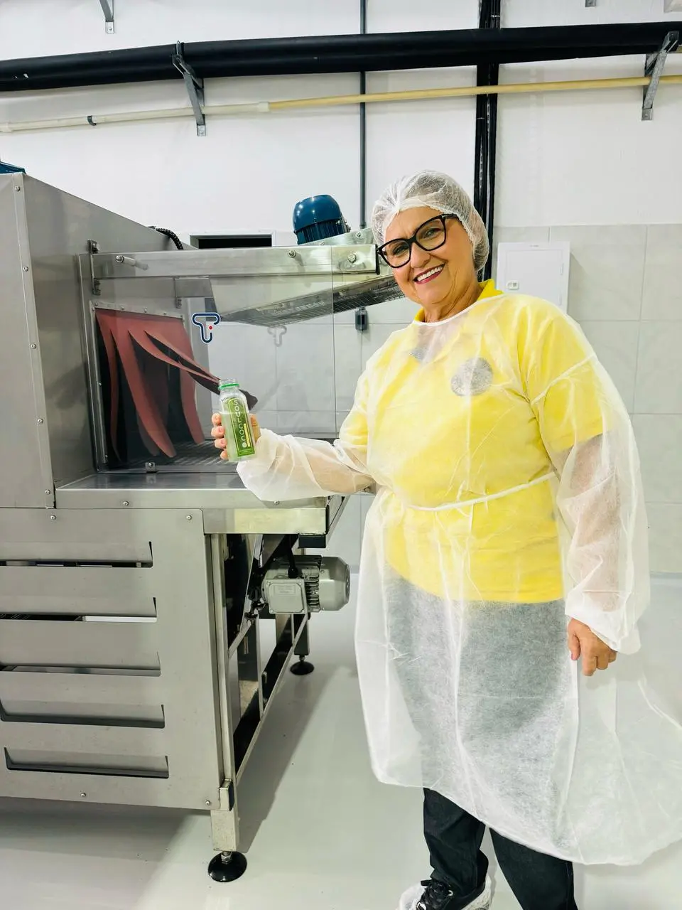 Imagem mostra mulher segurando uma garrafinha de água de coco em um ambiente que parece ser o de uma indústria