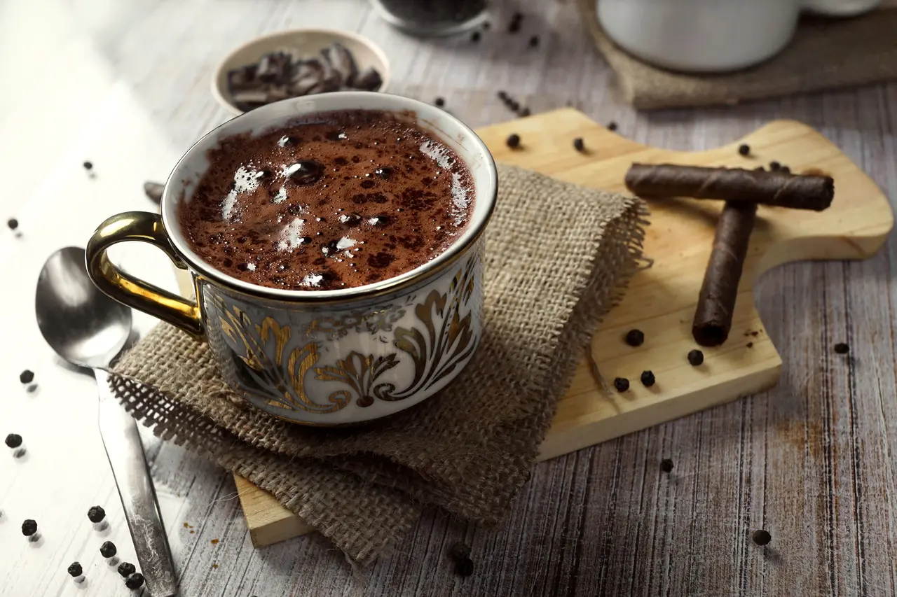 Imagem mostra xícara de chocolate quente sobre mesa de madeira, ilustrando receitas para esquentar frio no inverno 2025