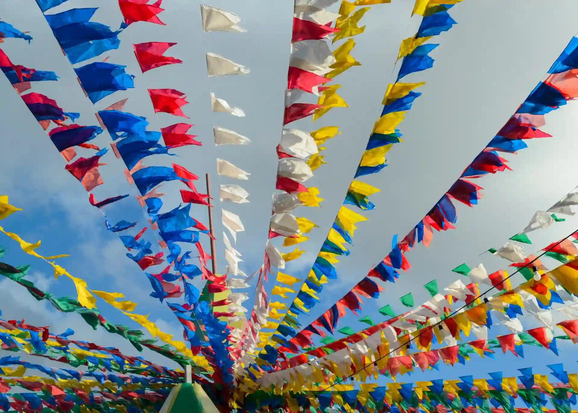 Decoração de festa com bandeirinhas coloridas em céu azul, representando o feriado de São João, que acontece no dia 24 de junho e é feriado em algumas capitais brasileiras.