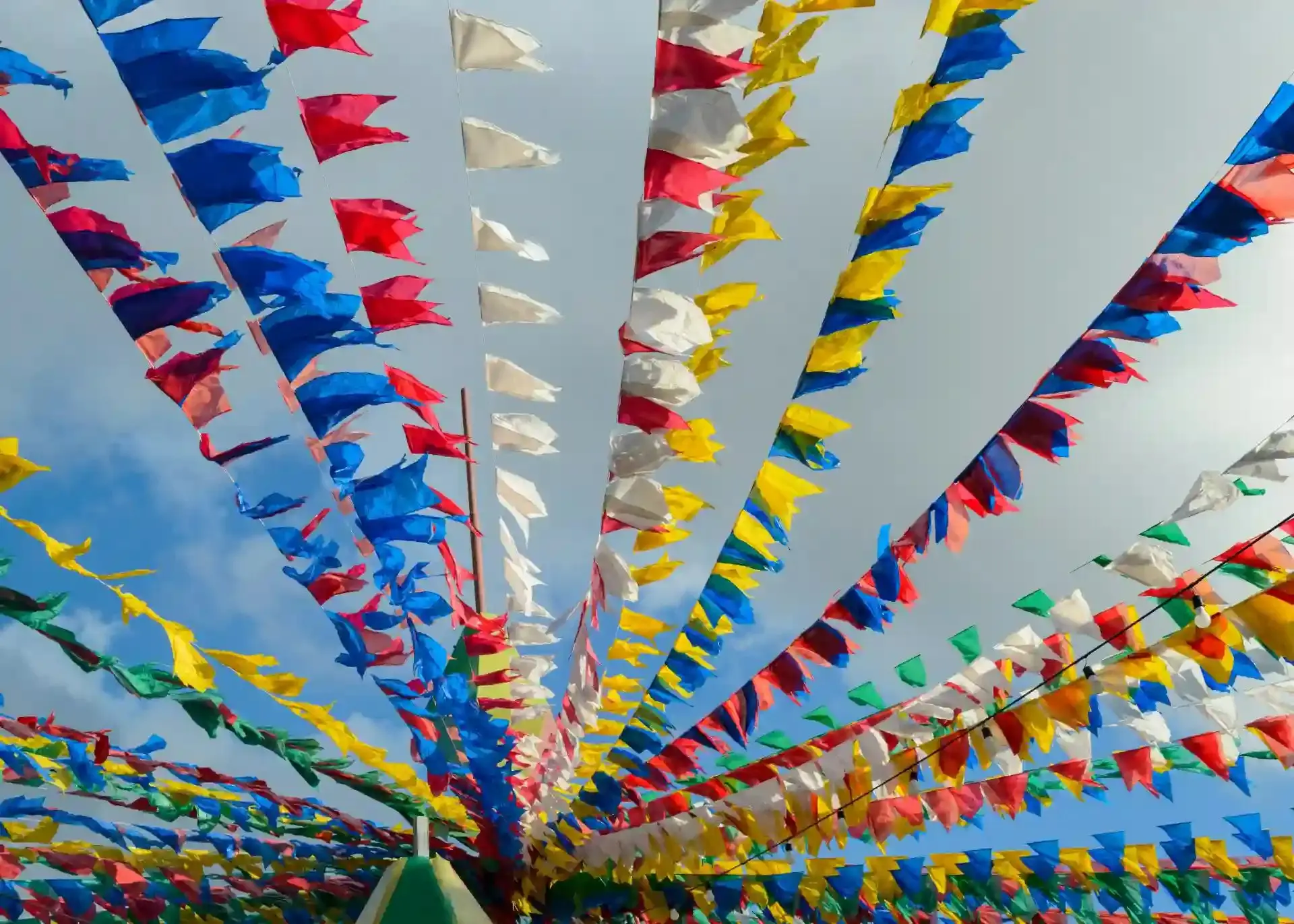 Decoração de festa com bandeirinhas coloridas em céu azul, representando o feriado de São João, que acontece no dia 24 de junho e é feriado em algumas capitais brasileiras.