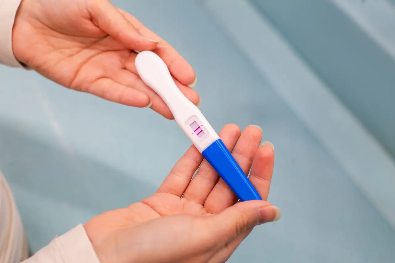 Imagem mostra close-up em mãos femininas segurando teste de gravidez positivo, ilustrando fenômeno chamado bebês ozempic