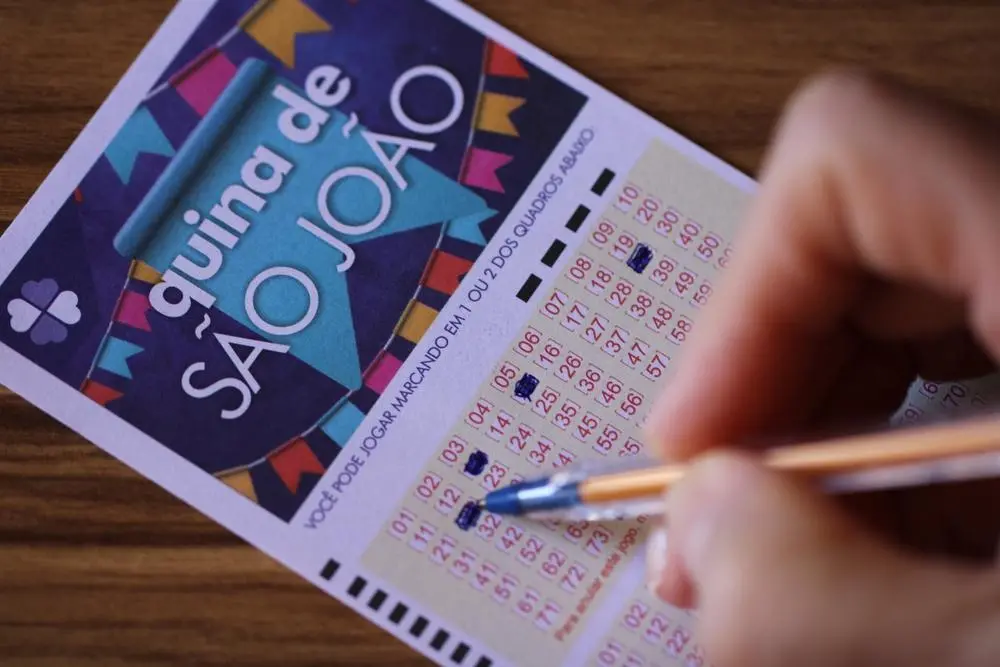 Imagem mostra close-up em mão preenchendo volante do concurso especial da Quina de São João, ilustrando números mais sorteados no resultado da Quina de São João