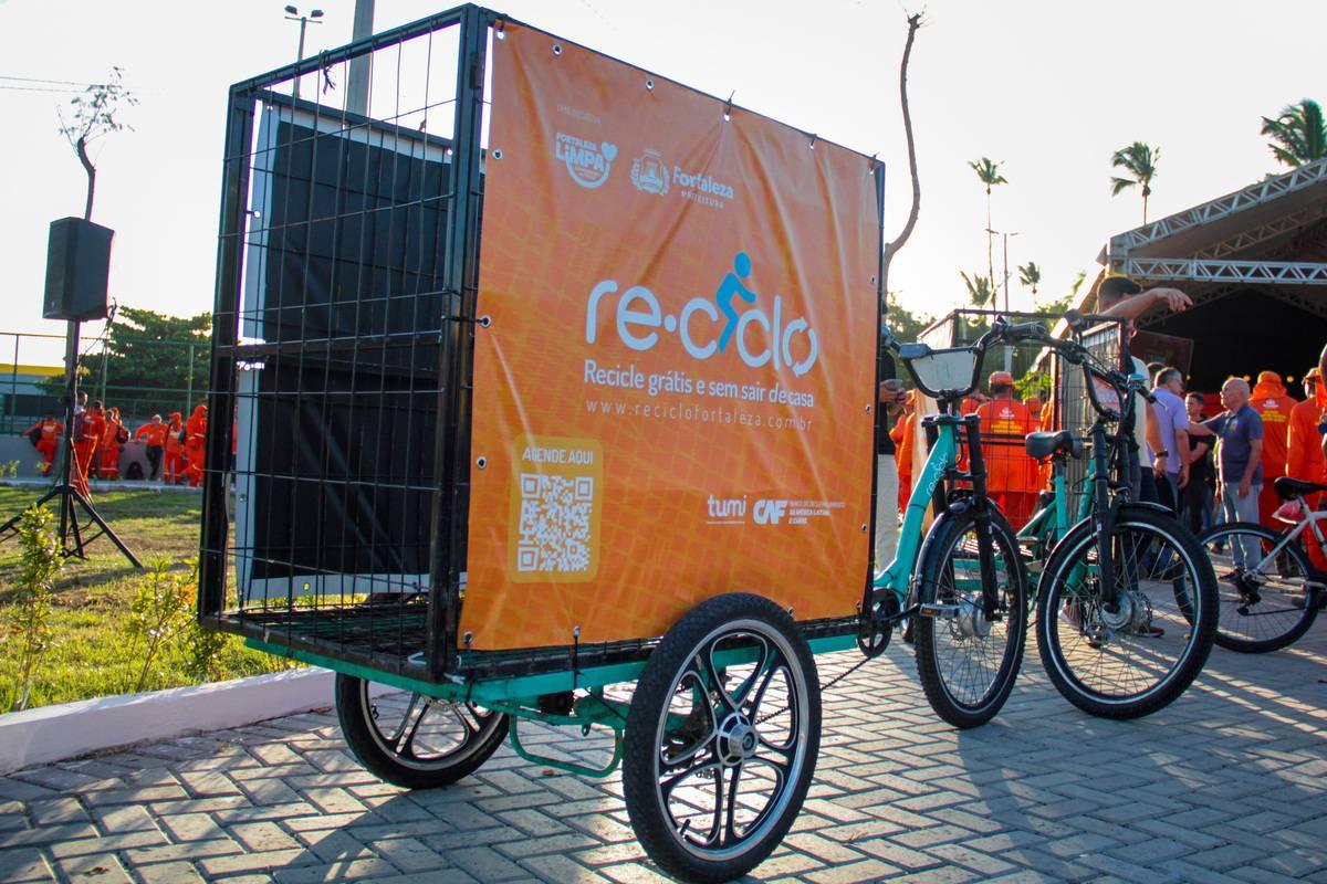 Uma bicicleta do projeto parada. Ela possui uma carroça e tem cores laranja e verde