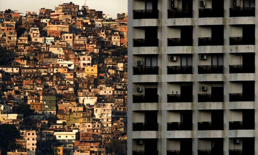 Imagem mostra a fachada de um prédio com uma favela atrás
