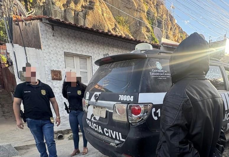 Policiais civis realizando procedimento em uma rua, com uma viatura da polícia ao fundo, durante o dia, em uma cidade no estado do Ceará.