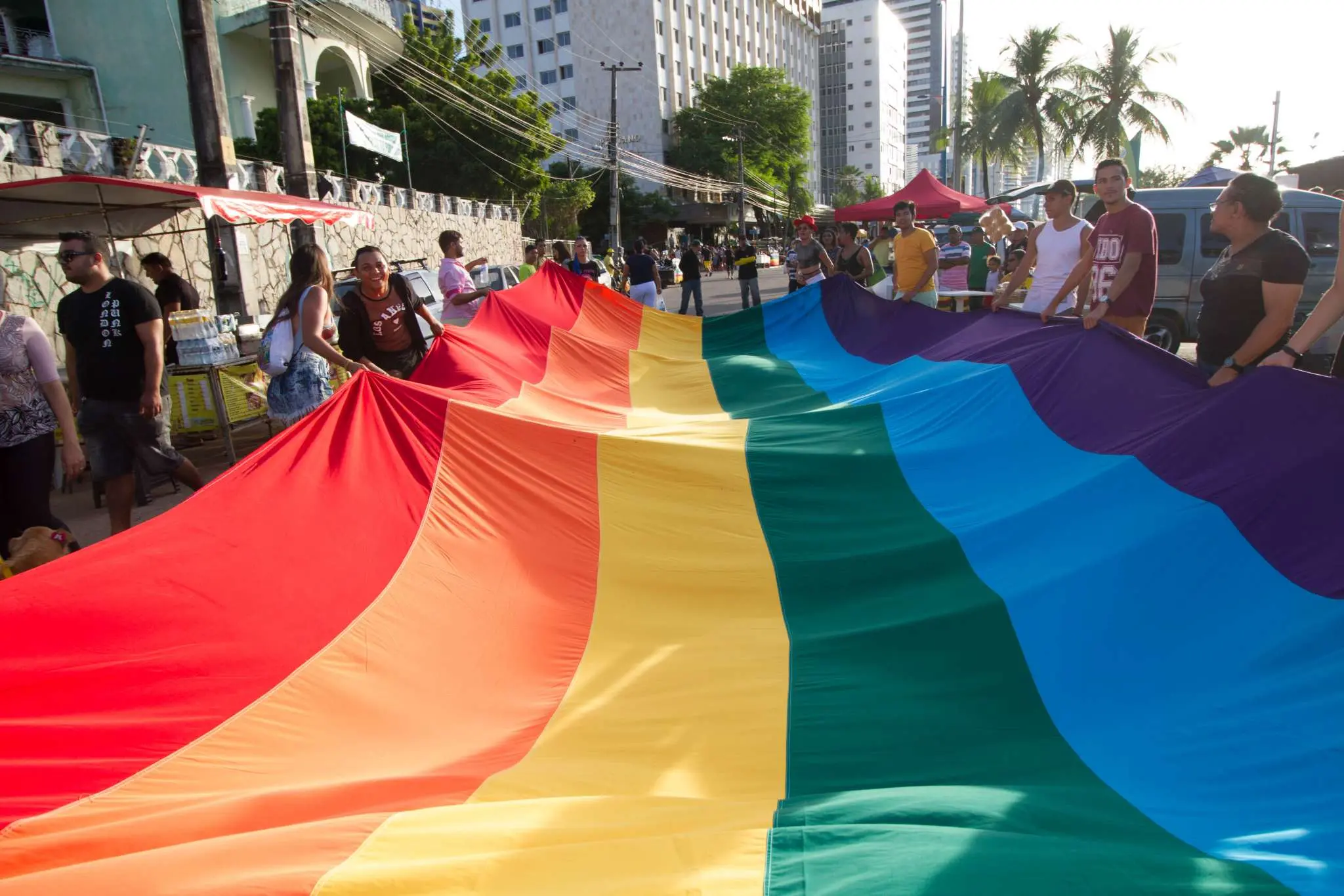 Imagem mostra grupo de pessoas segurando uma grande bandeira colorida, em referência à diversidade sexual