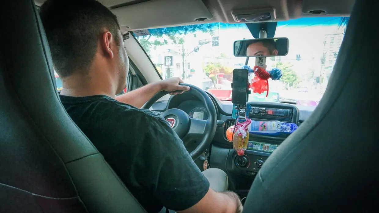 Foto mostra a partir interna de um carro, a partir da perspectiva de quem está sentado no banco de trás. Aparece um motorista ao voante nas ruas de Fortaleza