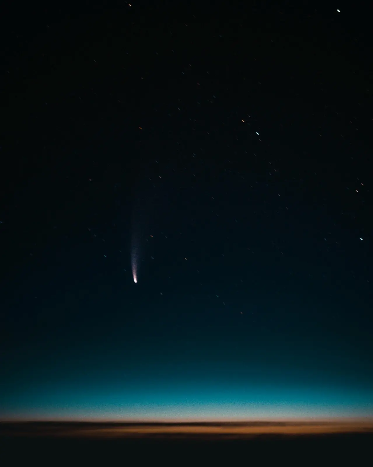 Céu noturno com estrelas e um cometa cruzando o horizonte iluminado ao fundo