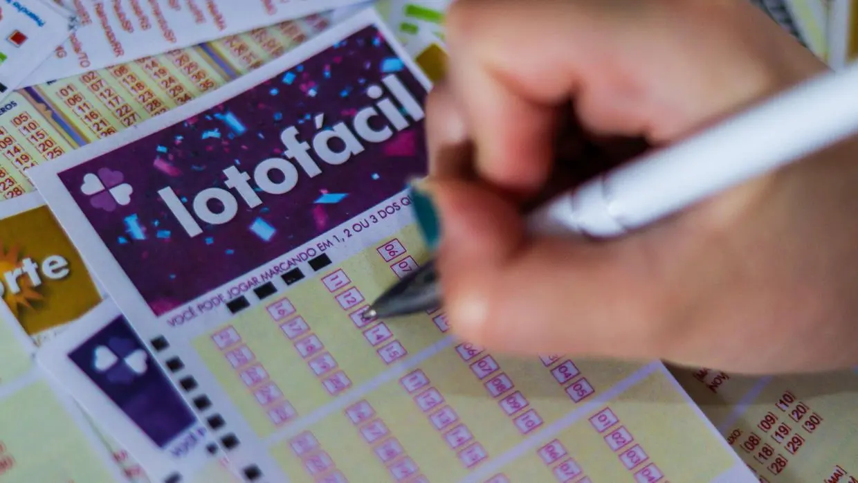 Pessoa marcando números em uma aposta da lotofácil, cercada por bilhetes de loteria e uma caneta na mão, ilustrando resultado com apostas vencedoras da Lotofácil 3430