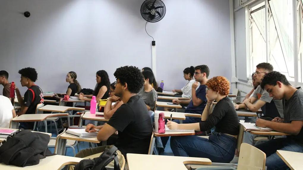 Estudantes em sala de aula com atenção focada na frente, sentados na cadeiras, com cadernos e garrafas de água, durante uma aula de preparação para o CNU 2025, ilustrando abertura das inscrições para o concurso.
