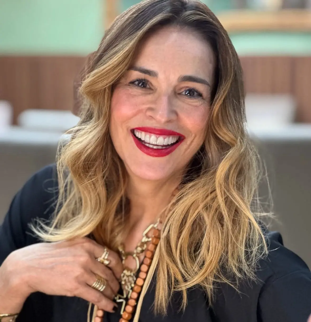 Suzy Rêgo é uma mulher branca e loira de cabelo ondulado. Na foto, ela está de batom vermelho