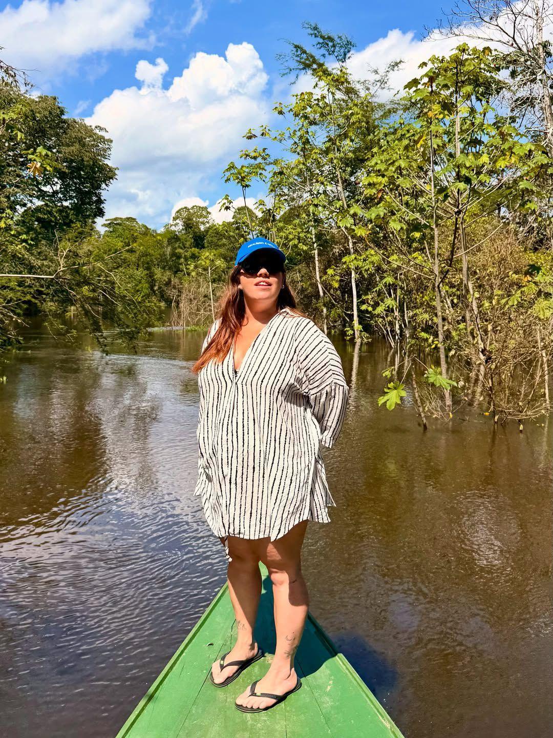 Tati Machado posando em barco, diante de floresta. ela veste camisa branca, óculos escuros e boné azul. em postagem nas redes, apresentadora relatou como tem sido resgatar a alegria