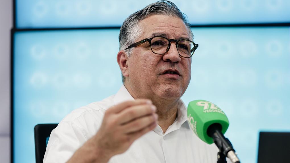 Imagem mostra o ministro da Saúde, Alexandre Padilha, em entrevista à Verdinha FM 92.5 e à TV Diário, diante de um microfone verde. Ao fundo, uma tela LED mostra um cenário azul. O ministro fala sobre ações voltadas à saúde pública do Ceará.