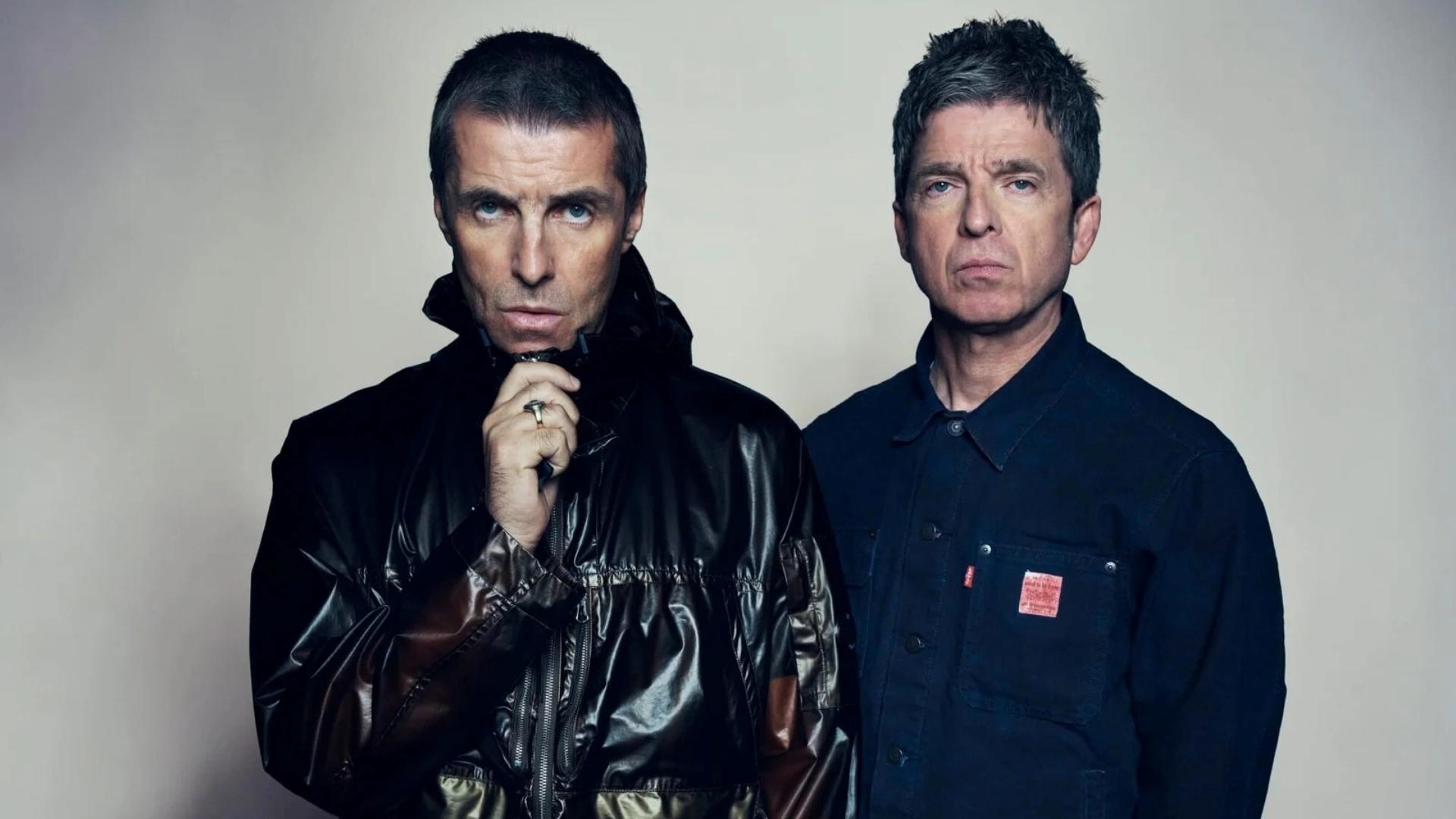 Foto dos integrantes da banda de rock Oasis, com fundo neutro, destaque para as expressões faciais marcantes de ambos e estilo casual.