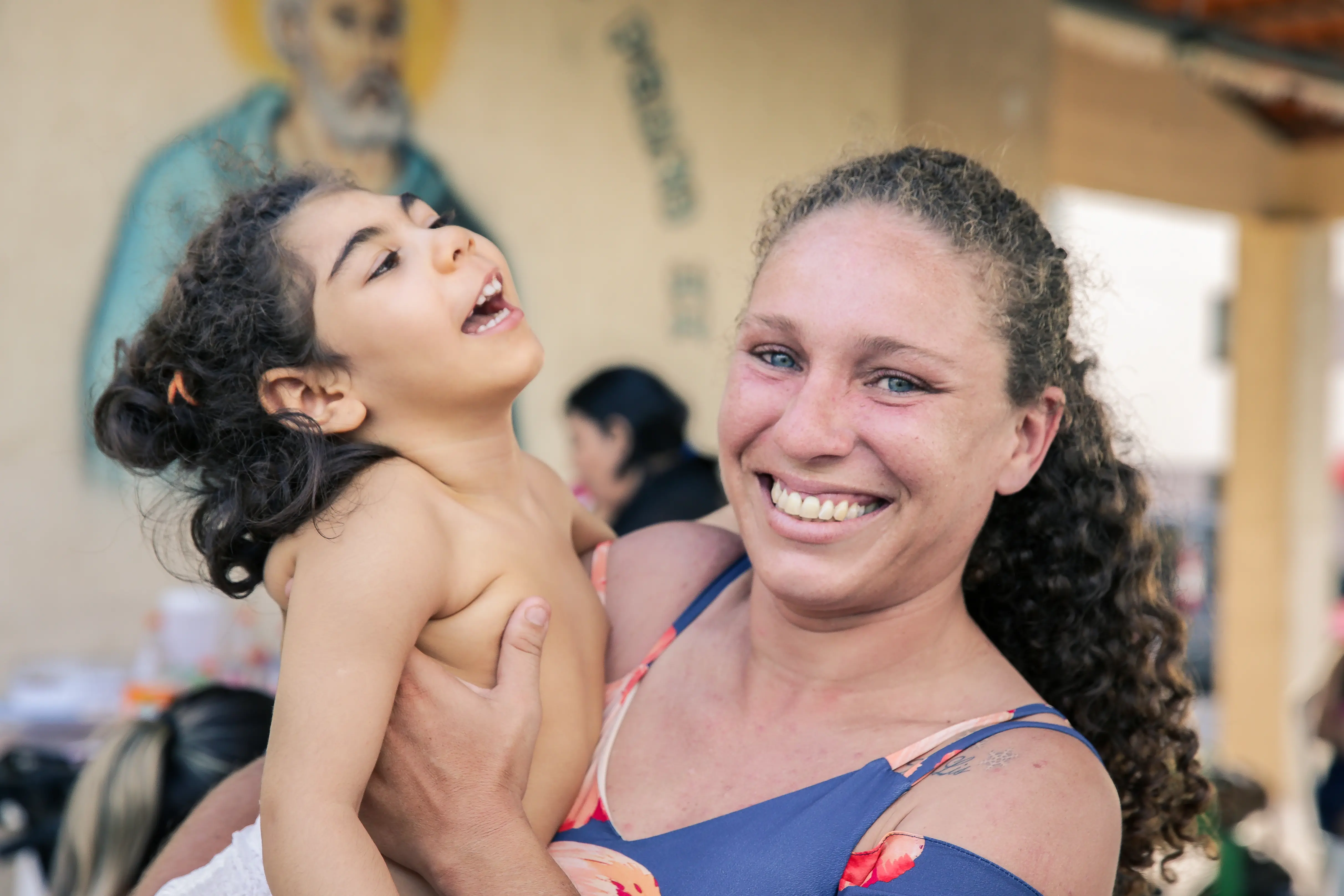 Uma pessoa está segurando uma criança no colo. A criança está sobre o ombro, e a pessoa que a segura aparece de lado, com o cabelo preso